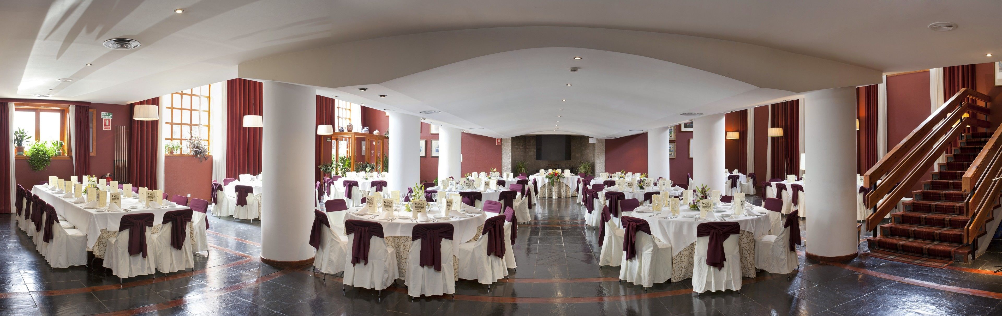 Une salle de banquet spacieuse, avec des tables rondes, des nappes blanches et des housses de chaise violettes.