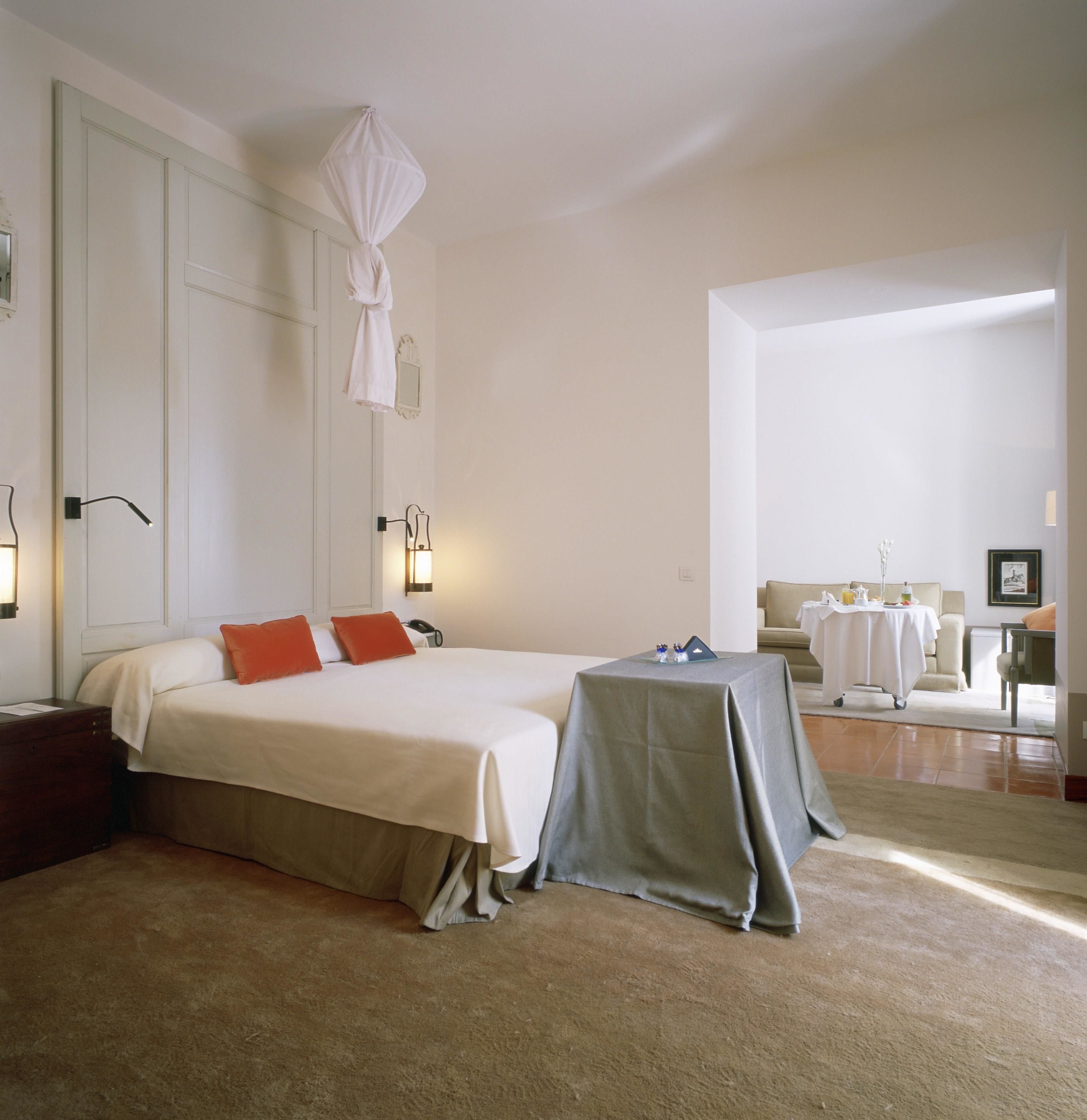 A hotel room with a large bed, a bedside table, a small table with a tablecloth, a chair, and a sofa.