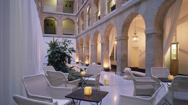 A spacious courtyard with wicker furniture and candles, surrounded by stone arches and a high ceiling with skylights. - Parador De La Granja (La Granja de San Ildefonso)