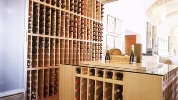 Una bodega con estanterías de madera llenas de botellas de vino, un porta copas de vidrio y un refrigerador.