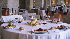 A restaurant with round tables set for dining, featuring white tablecloths, wine glasses, and plates of food. - Parador De La Granja (La Granja de San Ildefonso)