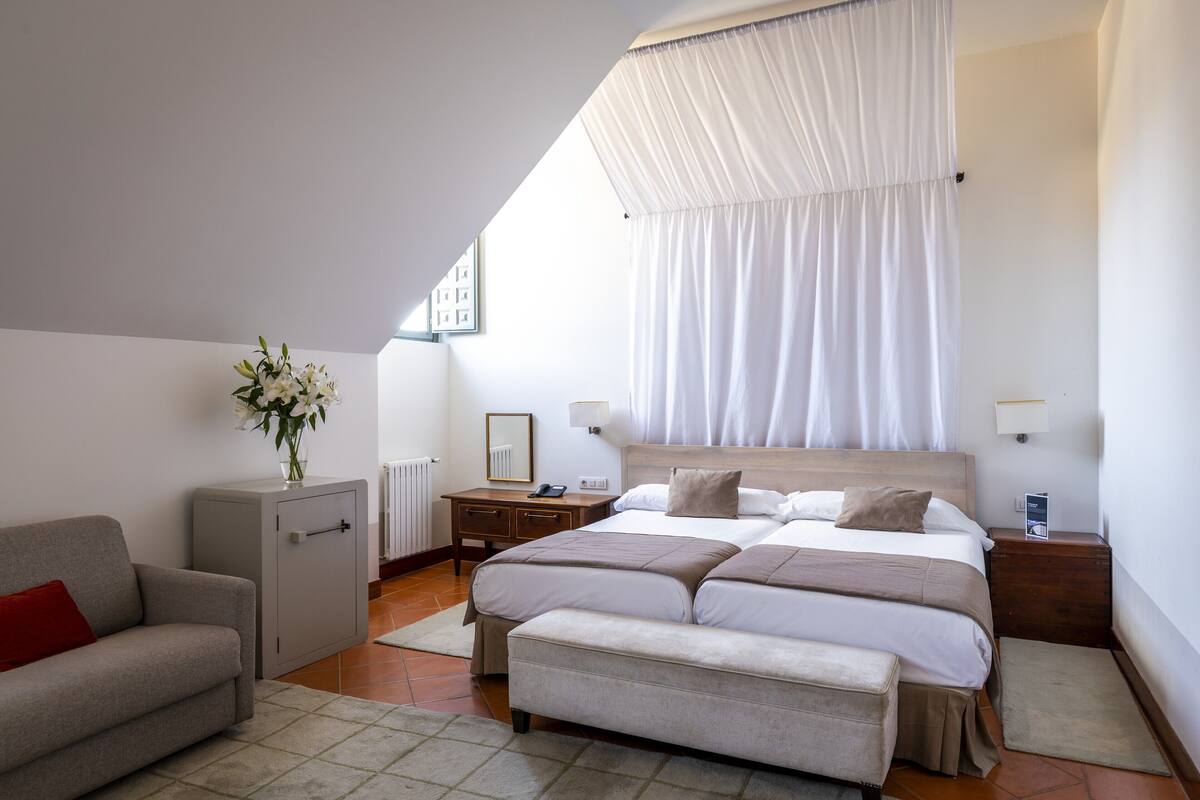 A bedroom with a bed, bedside tables, a nightstand, a sofa, a cabinet, and a window with curtains.