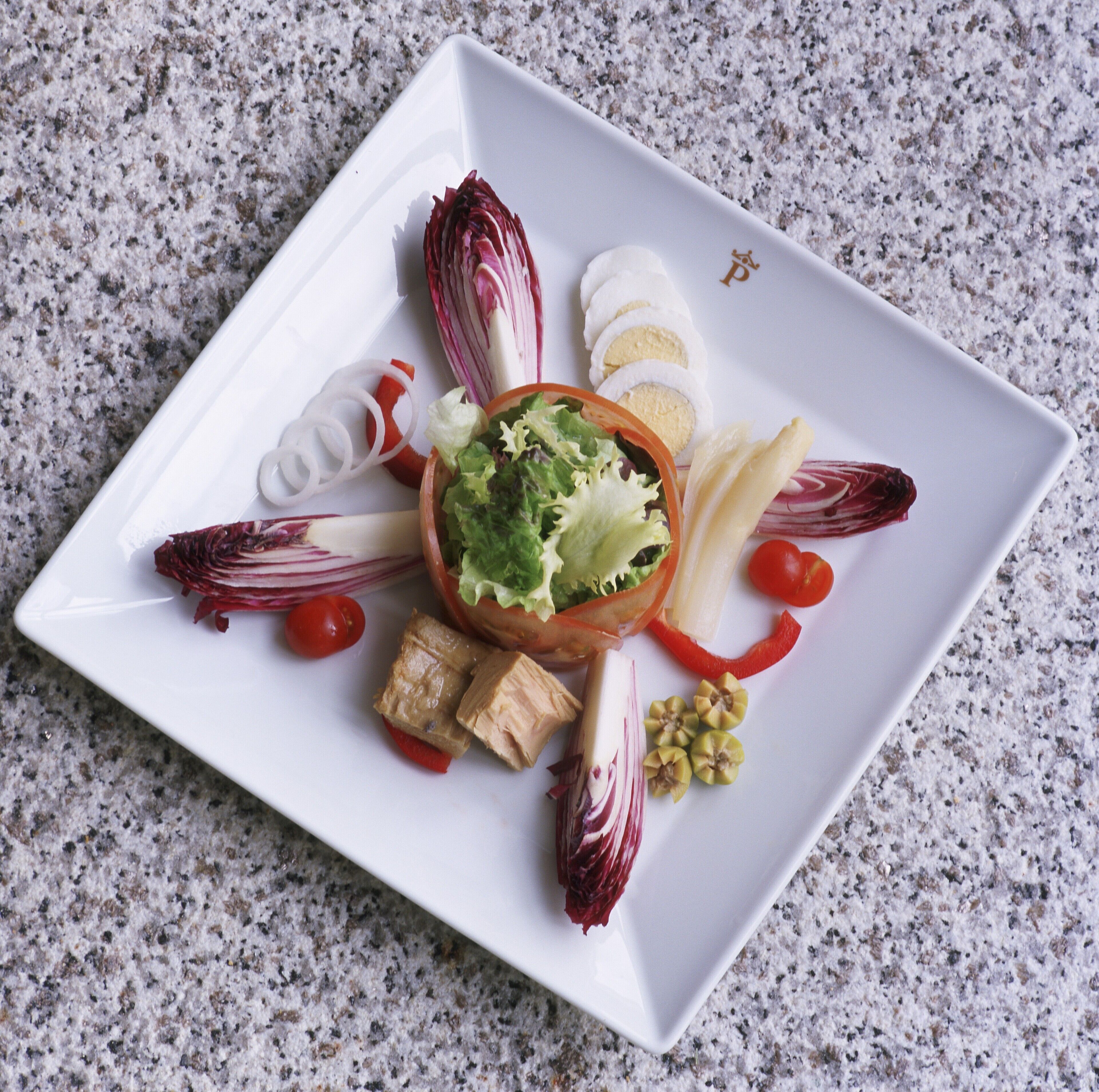 A square white plate with a variety of food items including lettuce, tomatoes, and other vegetables.