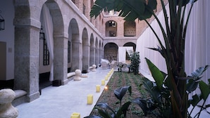 A courtyard with a central garden, stone arches, and a high ceiling with skylights. - Parador De La Granja (La Granja de San Ildefonso)