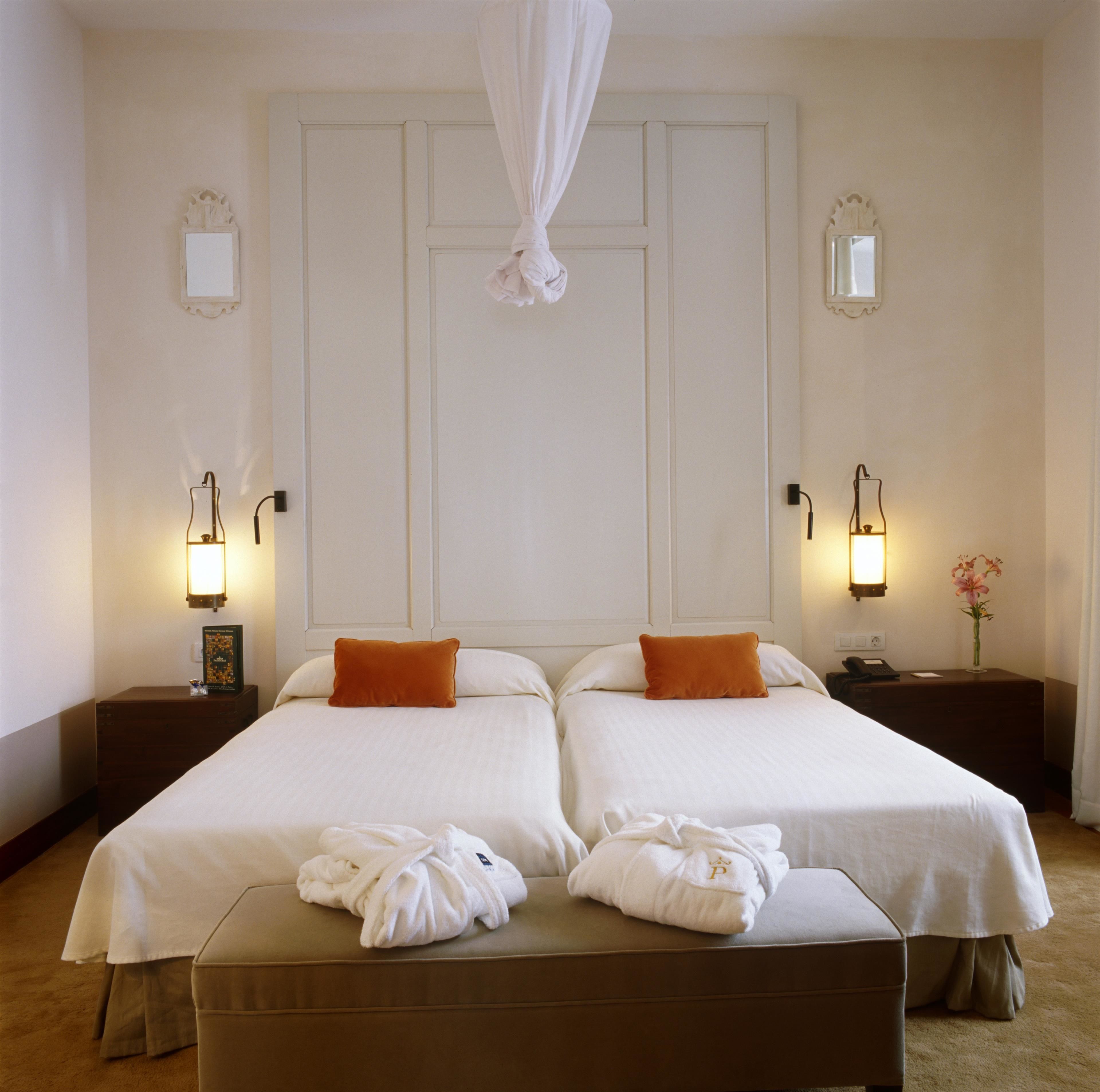 A hotel room with two beds, a large mirror, bedside lamps, and a bedside table with a vase of flowers.