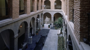 A spacious atrium with high ceilings, multiple levels of arches, and a central courtyard with a statue and potted plants. - Parador De La Granja (La Granja de San Ildefonso)