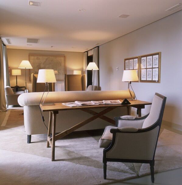 A hotel room with a large bed, two bedside tables, two lamps, a desk with a chair, a carpeted floor, and a wall with framed pictures.