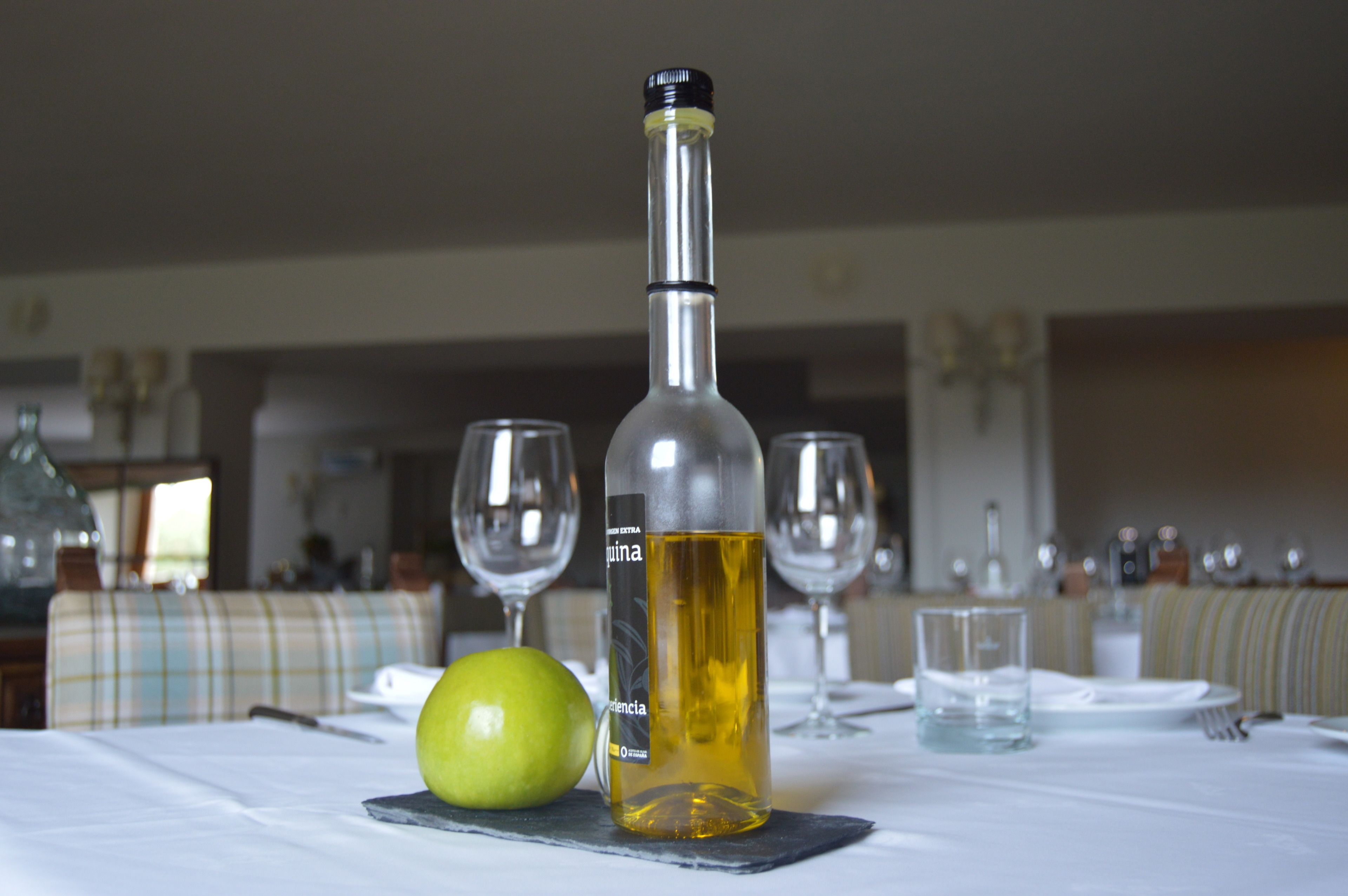 Una mesa de comedor con una botella de vino blanco, una copa y una manzana verde.