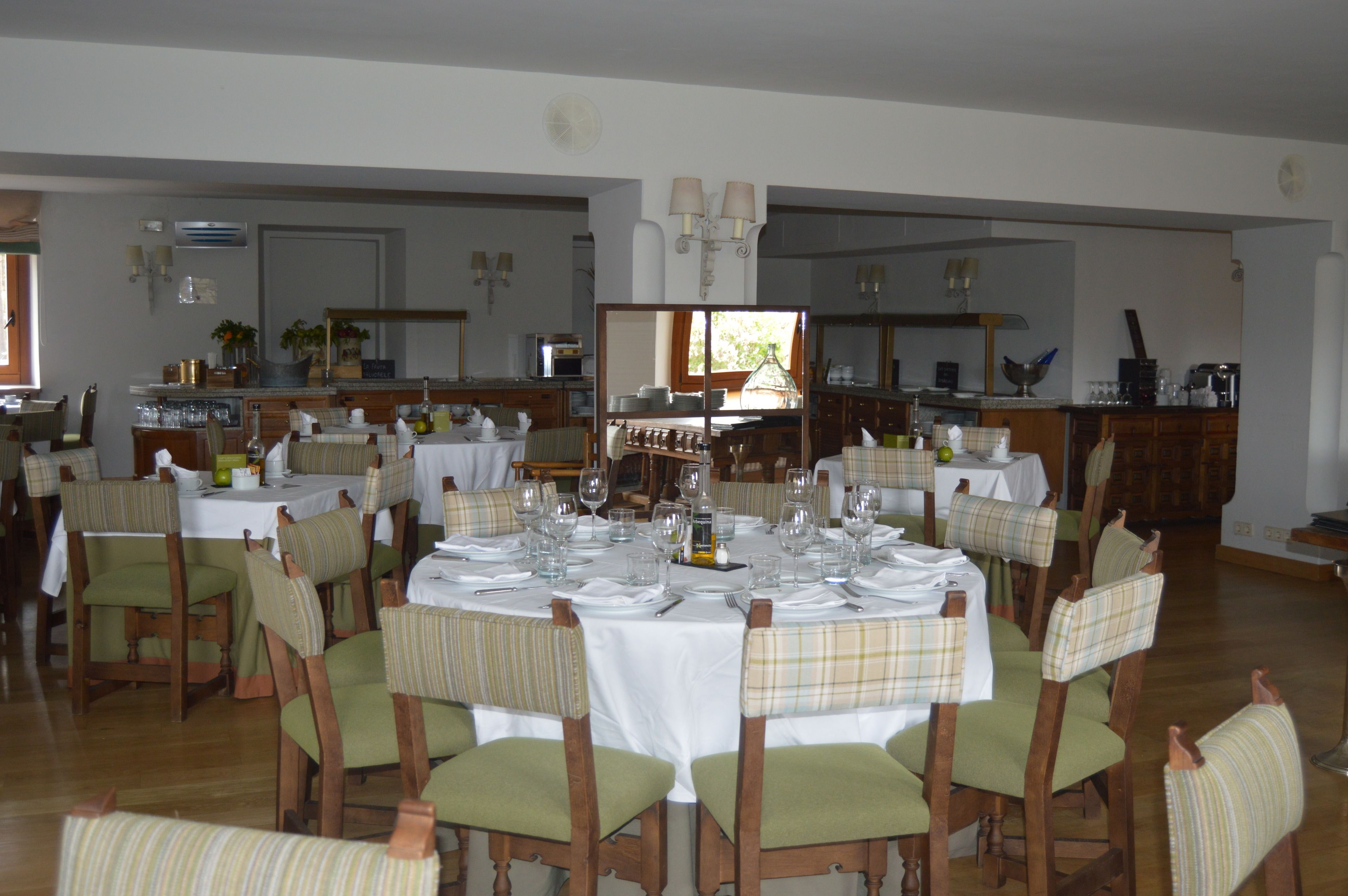 Comedor con mesas redondas dispuestas para varios comensales, rodeado de sillas tapizadas.