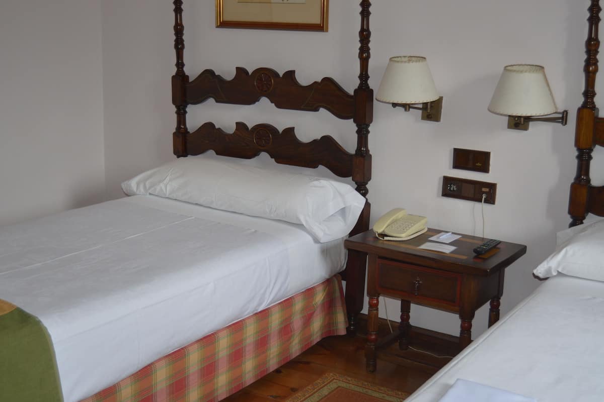A hotel room with a four-poster bed, a bedside table with a lamp, a telephone, and a small nightstand.