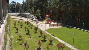 A playground with a slide and climbing structure, surrounded by a stone wall and a grassy area with small plants.