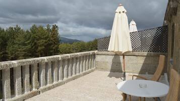 Una terraza en la azotea con barandilla de piedra, una mesa redonda, dos sillas de mimbre y dos sombrillas blancas.