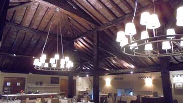 Un restaurante con varias mesas dispuestas para comer, techo alto con vigas a la vista y candelabros colgantes.