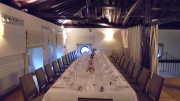 Una larga mesa de comedor preparada para una comida, con sillas a ambos lados, un mantel blanco y un techo de madera.