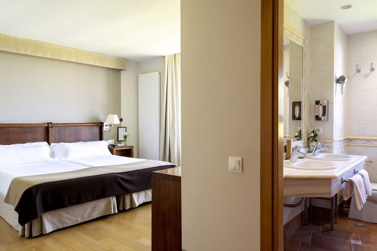 A hotel room with a bed, bedside table, lamp, and a bathroom with a sink and mirror.
