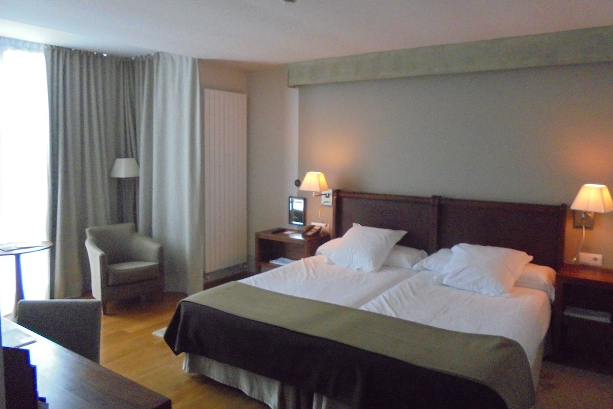 A hotel room with a large bed, two bedside tables with lamps, a chair, and a desk.