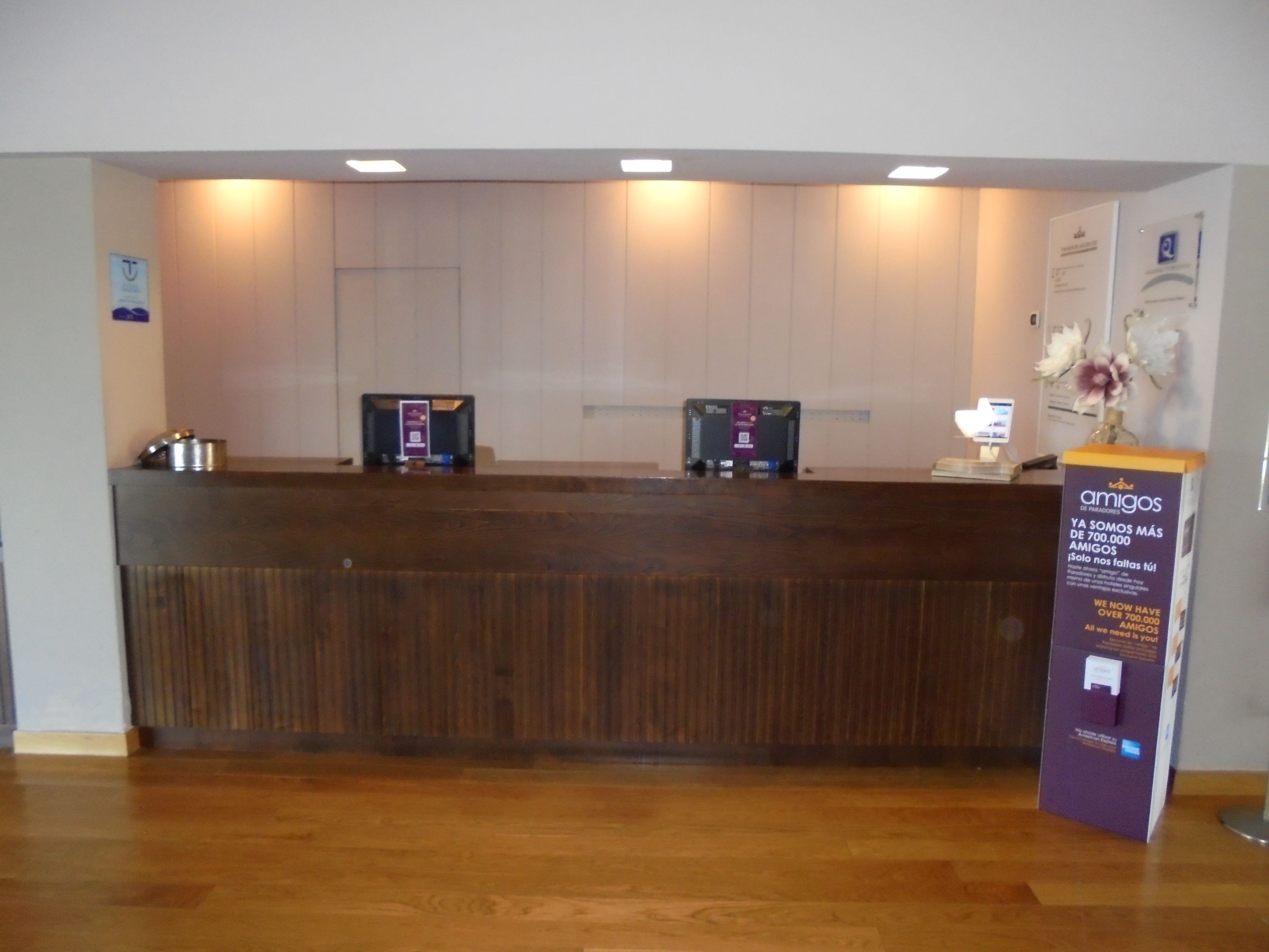 Un mostrador de recepción con detalles de madera, dos computadoras y un expositor púrpura de información.