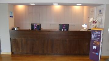 Un mostrador de recepción con detalles de madera, dos computadoras y un expositor púrpura de información.