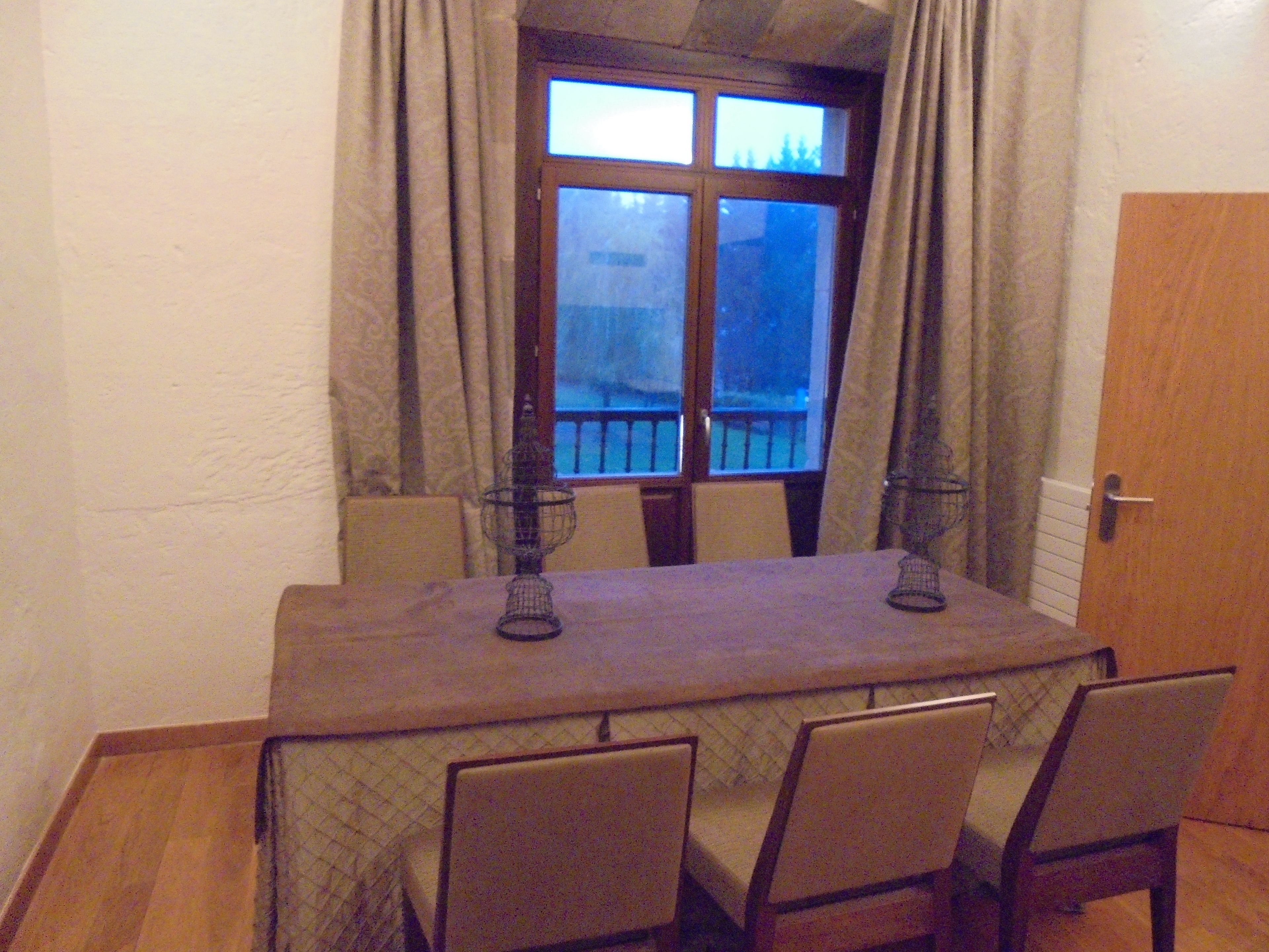 Una mesa de comedor con cuatro sillas, una ventana con cortinas y una puerta.