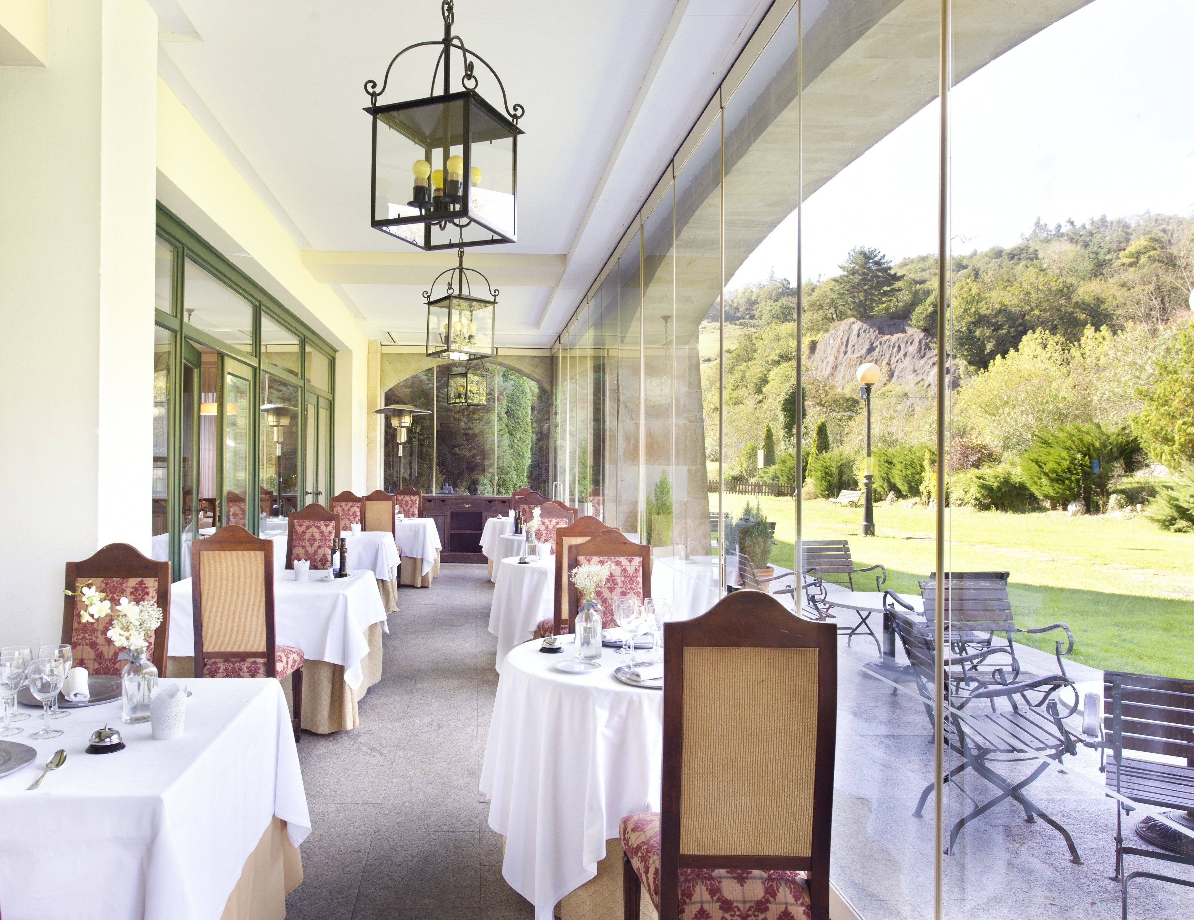 A restaurant with tables set for dining, large windows offering a view of the outdoors, and hanging lantern-style lighting fixtures.