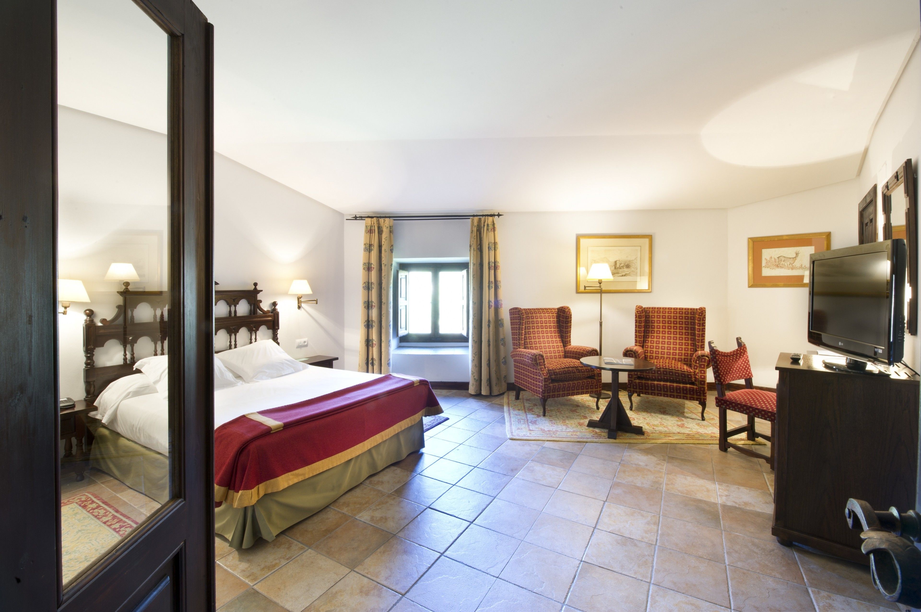 Ein Hotelzimmer mit einem Bett, einem Fernseher, einem Schreibtisch, zwei Stühlen und einem fenster mit Vorhängen.