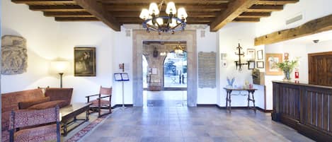 A lobby with a wooden ceiling, a chandelier, a reception desk, and a seating area with patterned chairs.