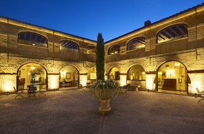Un patio con muros de piedra, arcos y una jardinera central con flores.