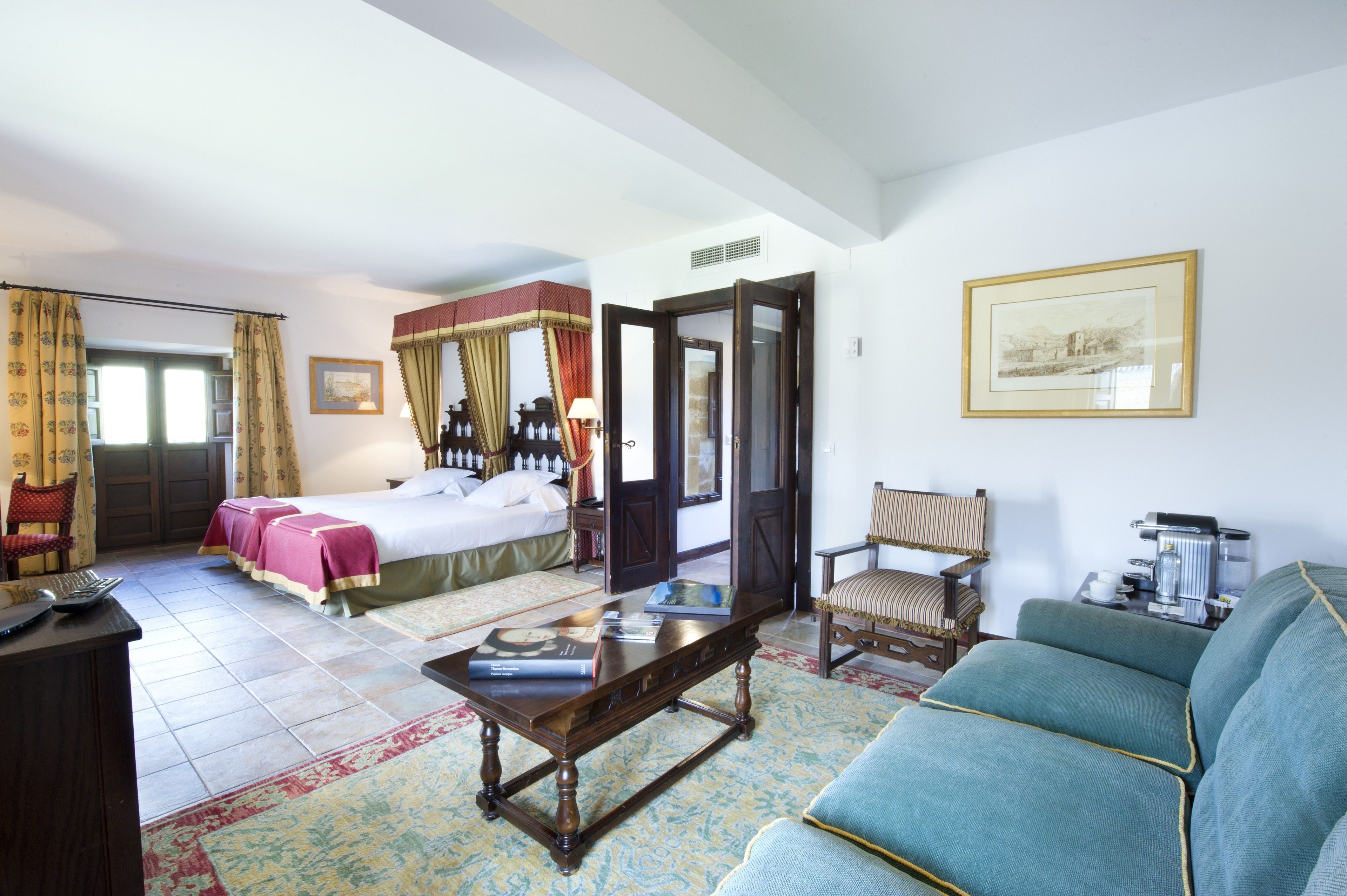 Habitación de hotel con cama, zona de estar con sofá y sillones, una mesa de centro y un escritorio con teclado.