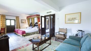 Habitación de hotel con cama, zona de estar con sofá y sillones, una mesa de centro y un escritorio con teclado.