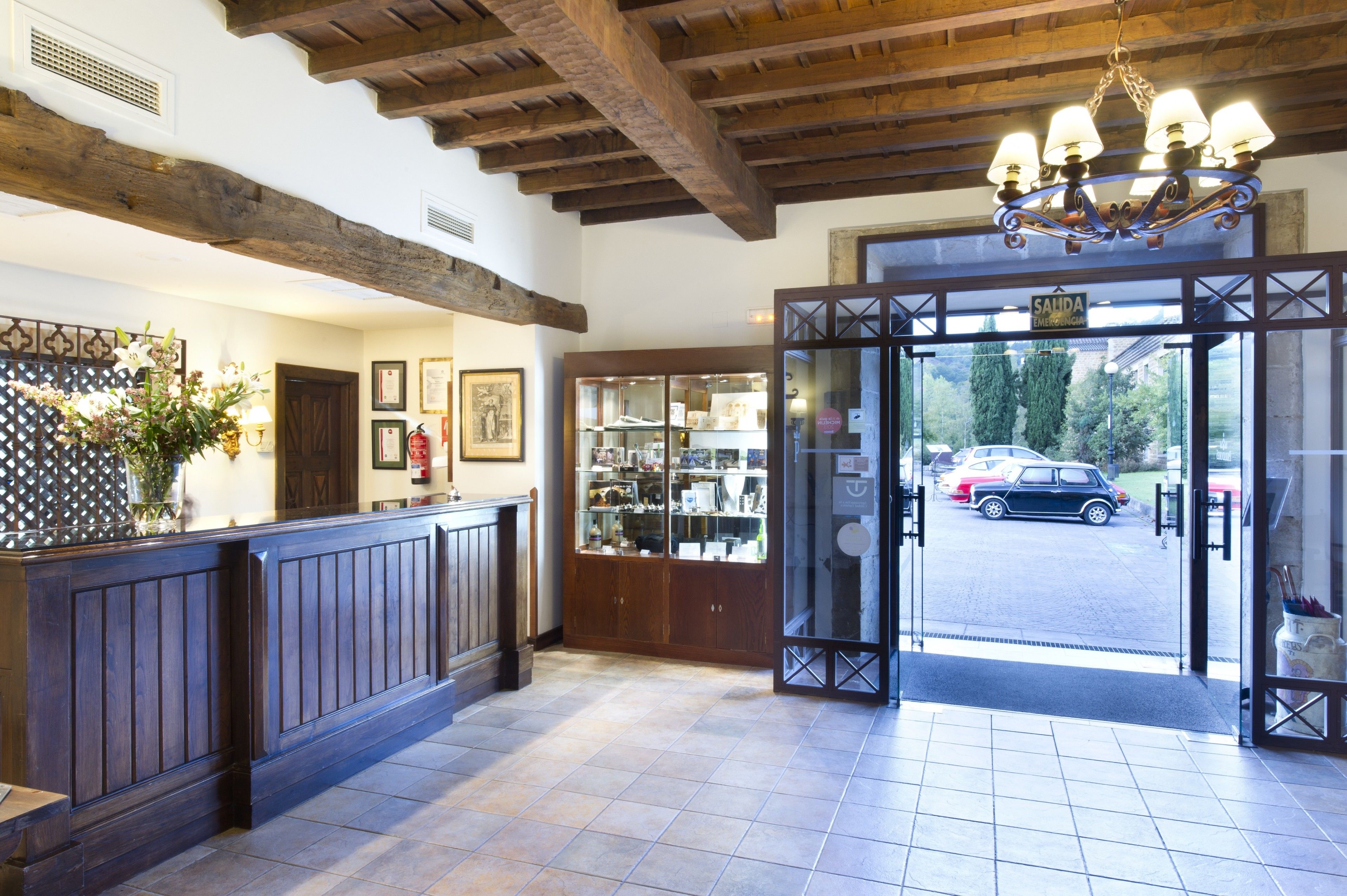 A reception area with a wooden reception desk, a chandelier, and a view of parked cars outside.