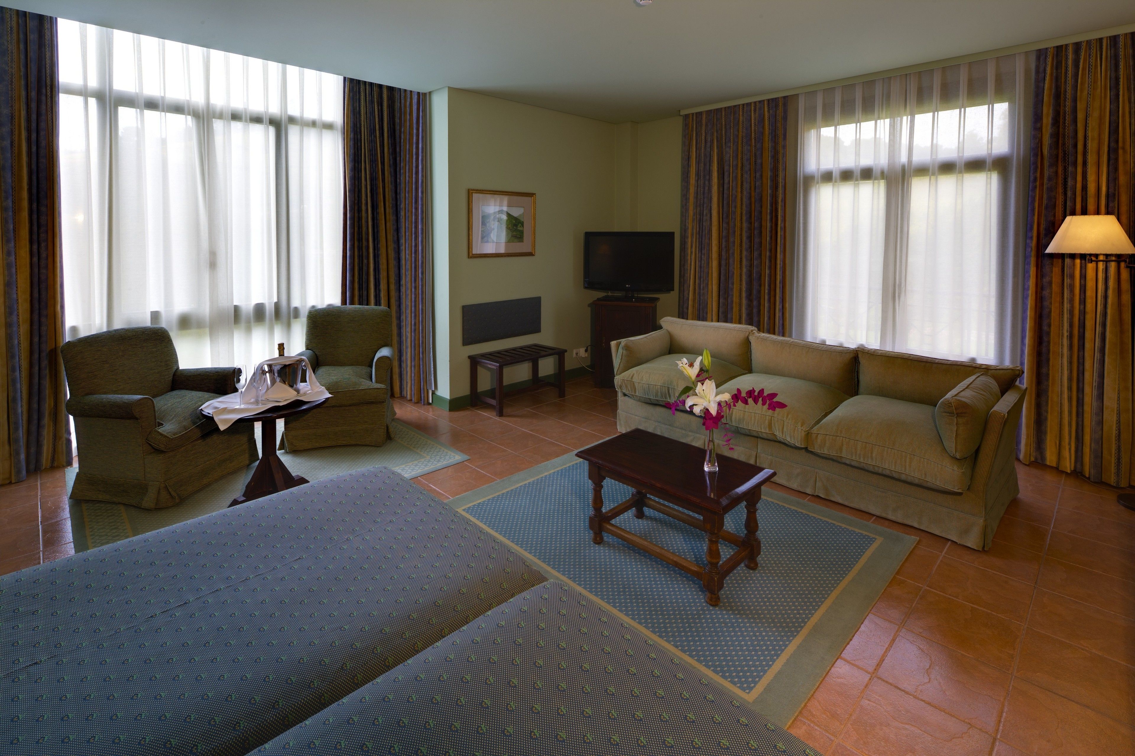 A hotel room with a sofa, two armchairs, a small table, a TV, and a lamp.