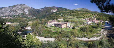 Un paisaje montañoso con un río, un puente y un conjunto de edificios con varias estructuras.