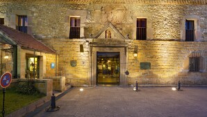 A stone building with a tiled roof, a central entrance, and a small garden area. - Parador De Cangas De Onis (Cangas de Onis)