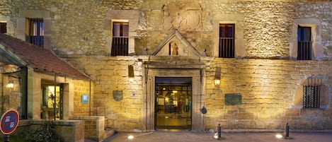 Un bâtiment en pierre avec un toit recouvert de tuiles, une entrée centrale et un petit jardin.