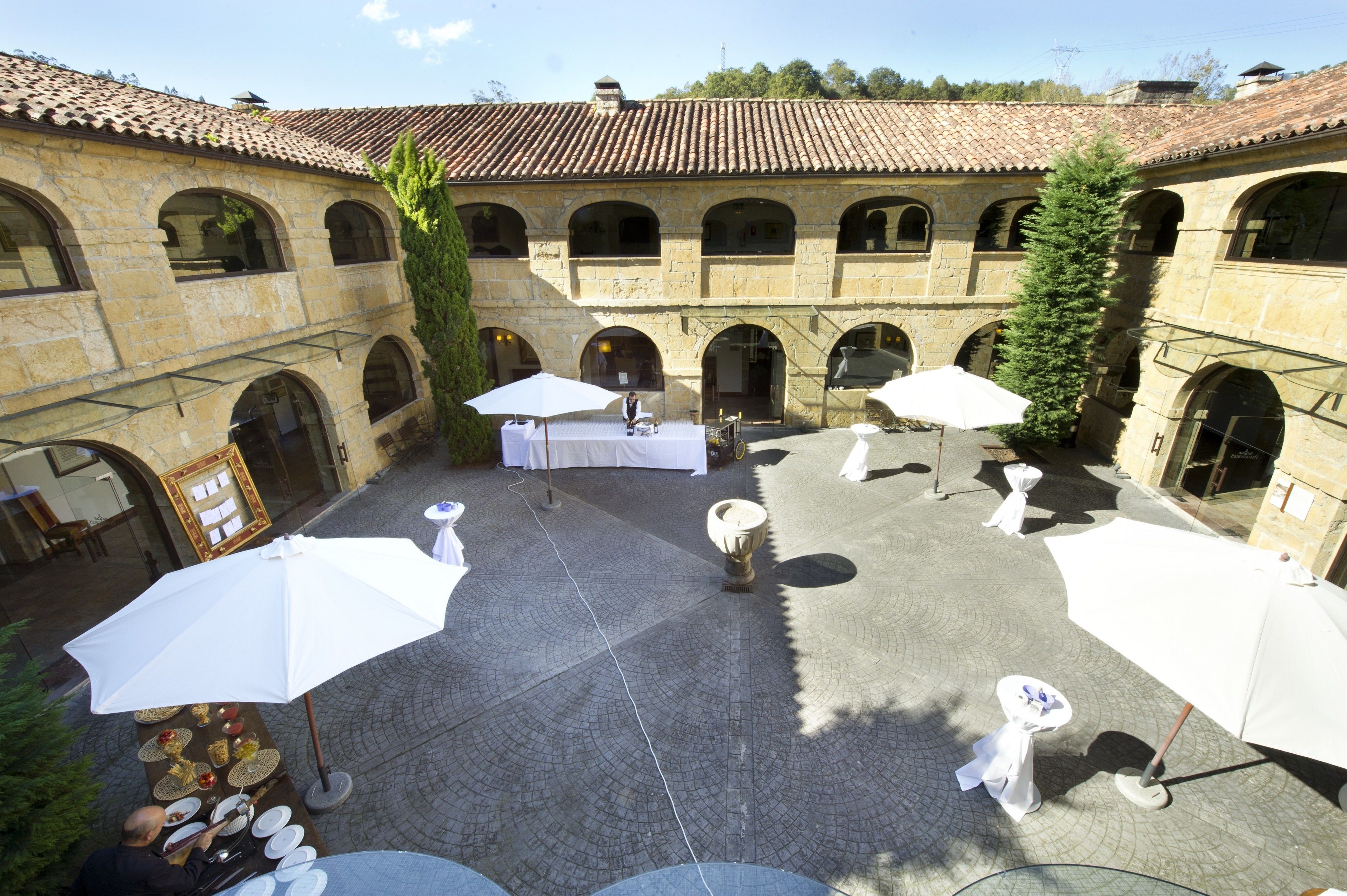 Un patio con mesas y sombrillas, paredes de piedra y techo de tejas.