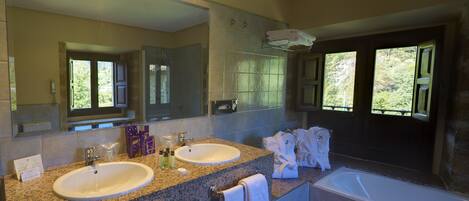 A bathroom with two sinks, a large mirror, a bathtub, and a view of the outdoors through the windows.