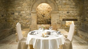 A stone-walled dining area with a round table set for two, featuring white tablecloths, candles, and a vase with flowers. - Parador De Cangas De Onis (Cangas de Onis)