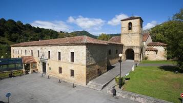 A historic stone building with a bell tower, a paved courtyard, and a grassy area.