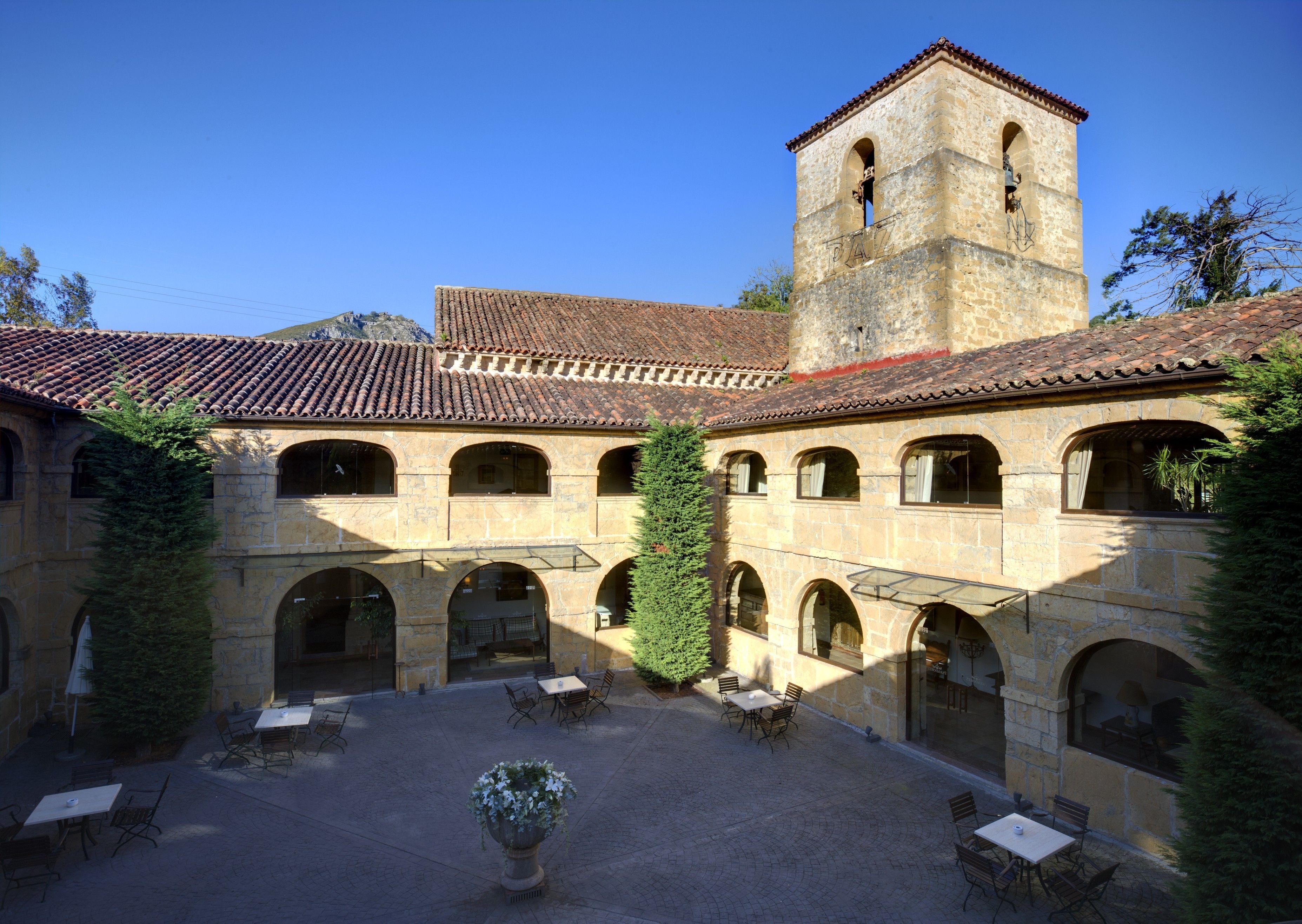 A courtyard with stone buildings, a bell tower, and outdoor seating.