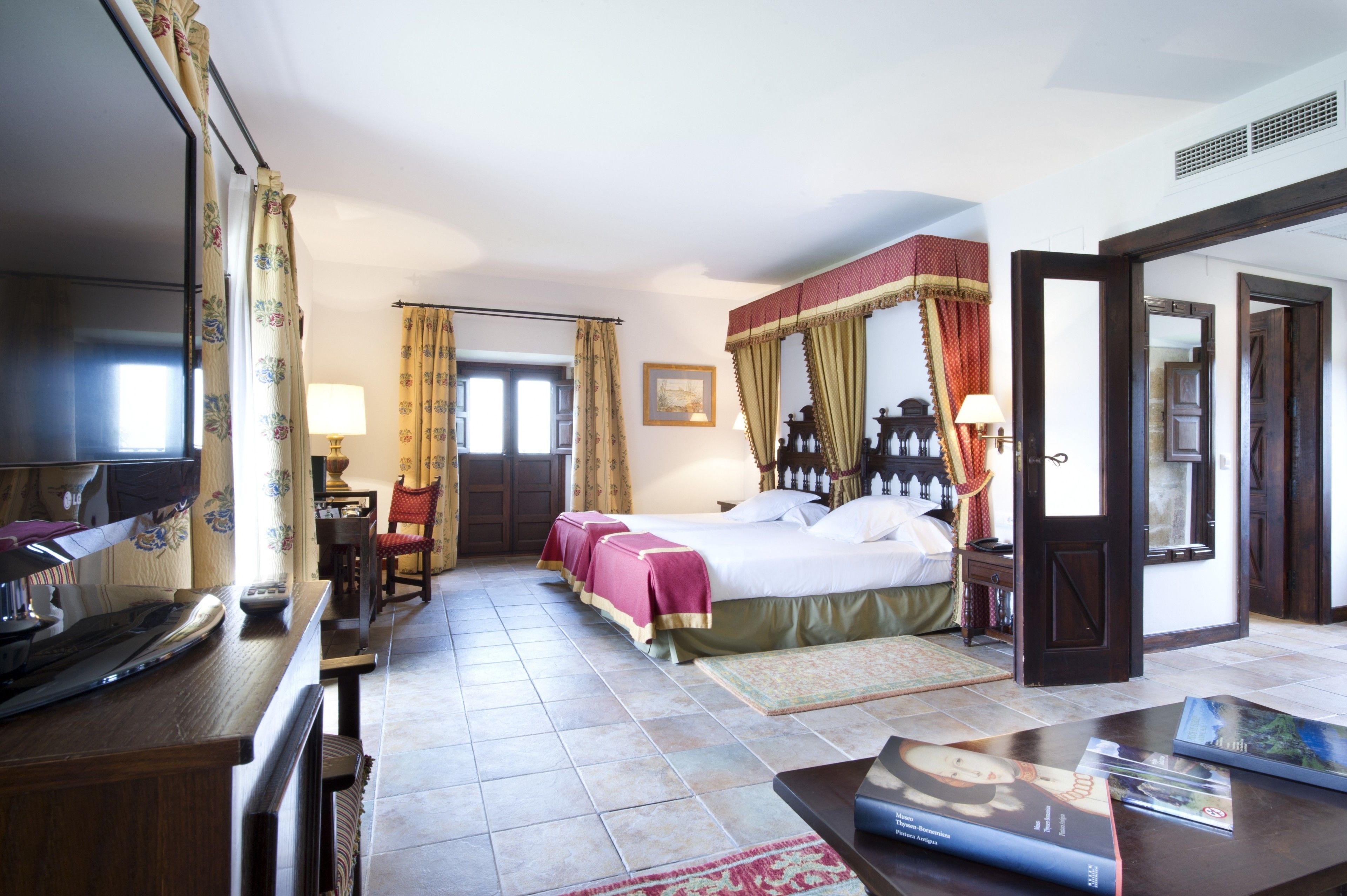 Habitación de hotel con cama, escritorio, silla, televisor y puerta.