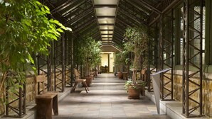 A covered walkway with potted plants and benches, leading to a door at the end. - Parador De Cangas De Onis (Cangas de Onis)