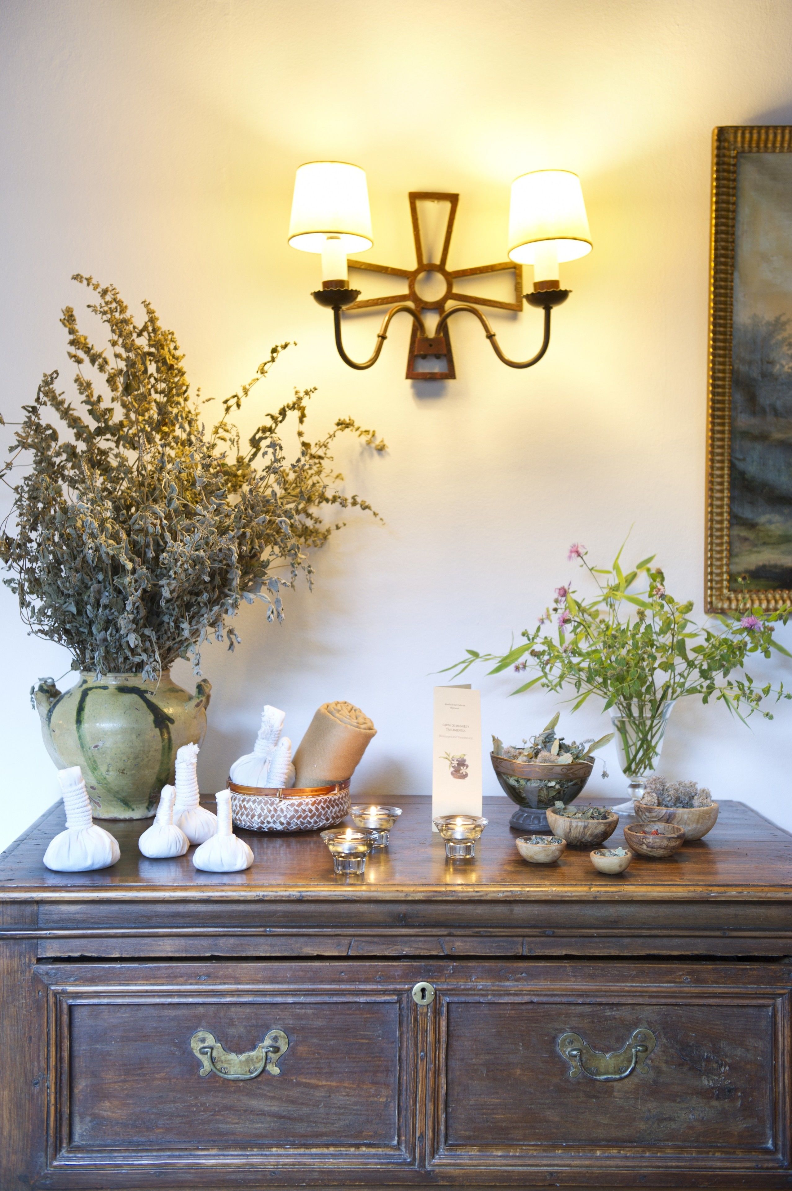 A wooden dresser with a vase of dried flowers, a small bowl, and a candle.