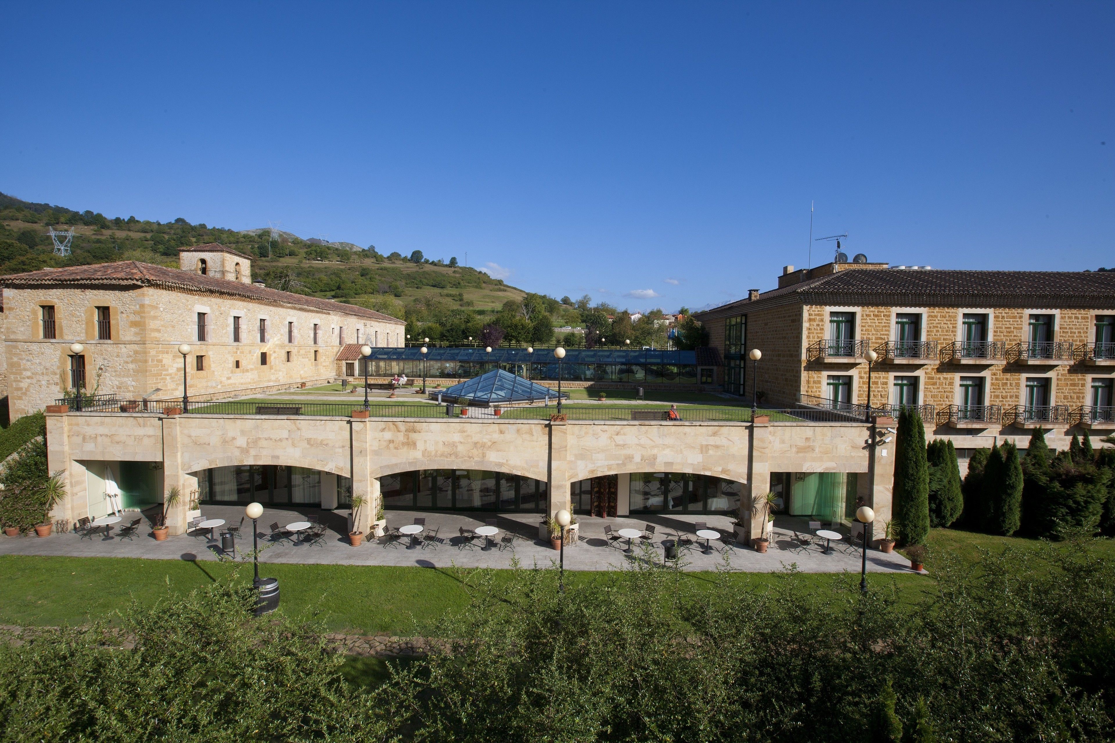 Une cour avec des espaces de repos en plein air, un pont de pierre et des bâtiments dotés de nombreuses fenêtres et de balcons.