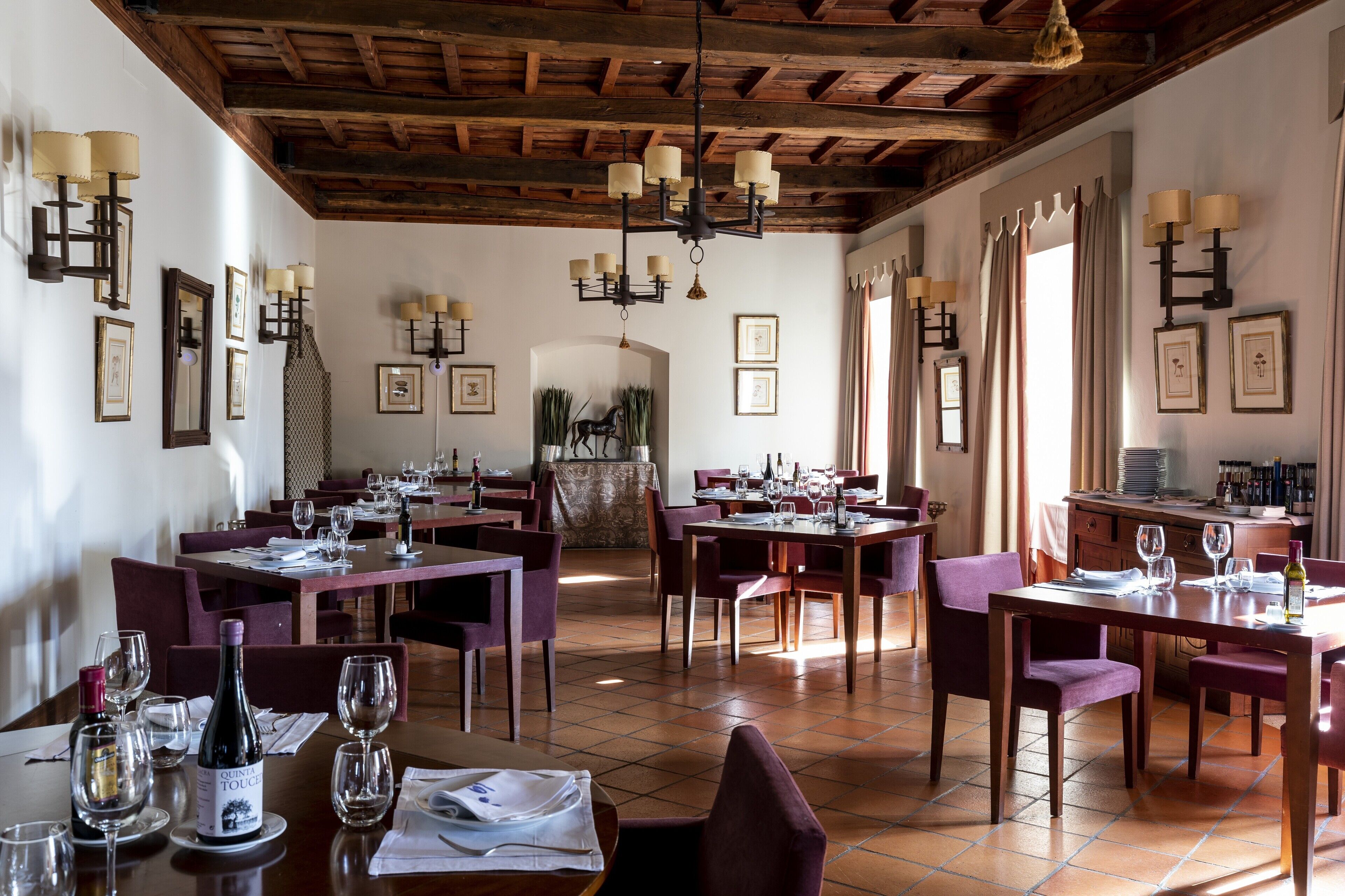 A restaurant with multiple tables and chairs, wooden beams on the ceiling, and framed pictures on the walls.