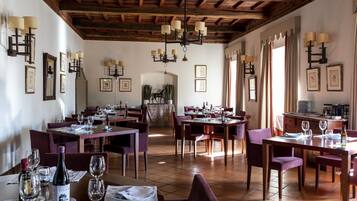 A restaurant with multiple tables and chairs, wooden beams on the ceiling, and framed pictures on the walls.