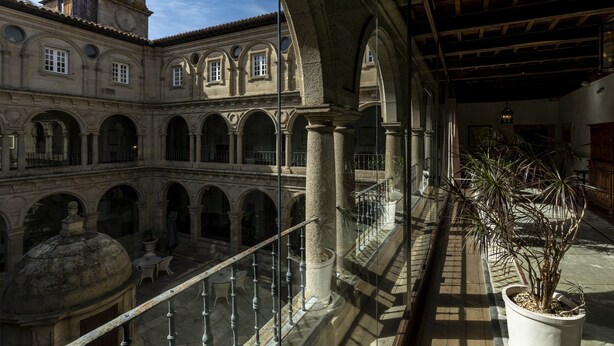 A courtyard with stone arches, a clock tower, and a potted plant. - Parador De Monforte De Lemos (Monforte de Lemos)