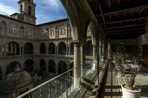 A courtyard with stone arches, a clock tower, and a potted plant. - Parador De Monforte De Lemos (Monforte de Lemos)