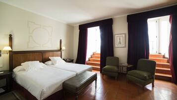 Een hotelkamer met twee bedden, een bankje, een stoel, een klein tafeltje en een trap.