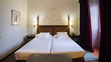 A double bed with a wooden headboard, two bedside tables with lamps, a framed picture on the wall, and a red curtain partially drawn.