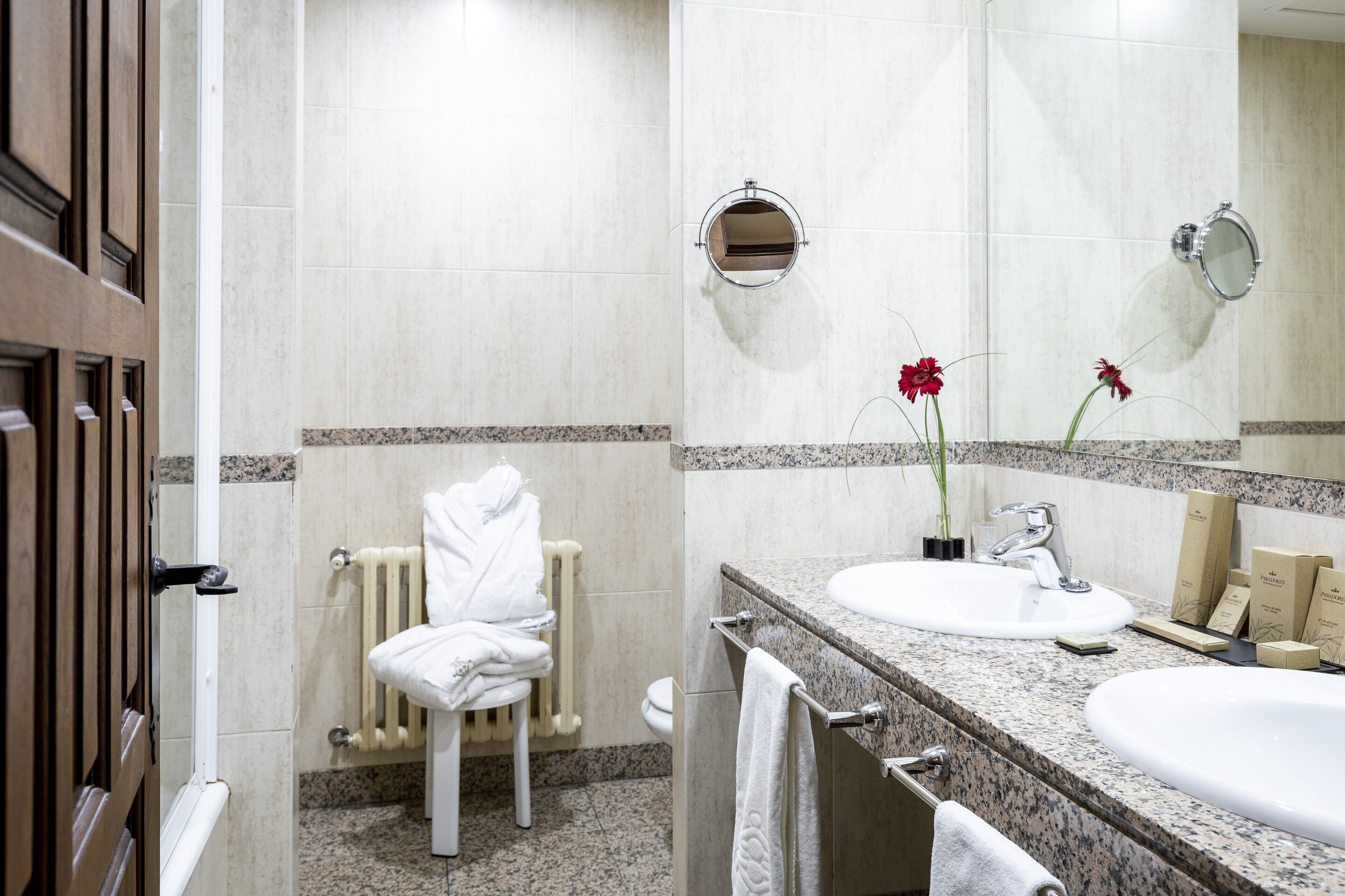 A hotel bathroom with a white sink, a mirror, a towel rack, and a radiator.